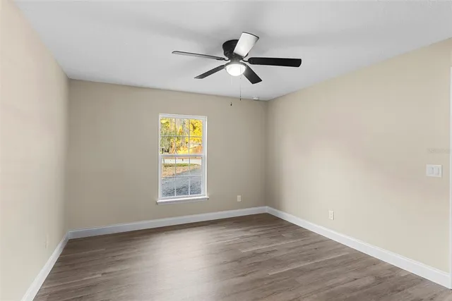 an empty room with wooden floor ceiling fan and windows