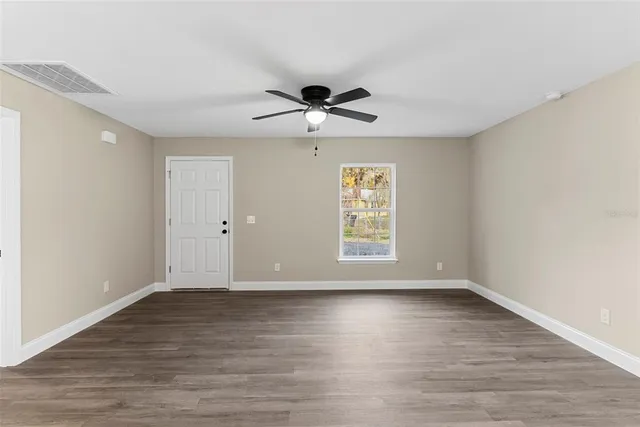 an empty room with wooden floor chandelier fan and windows