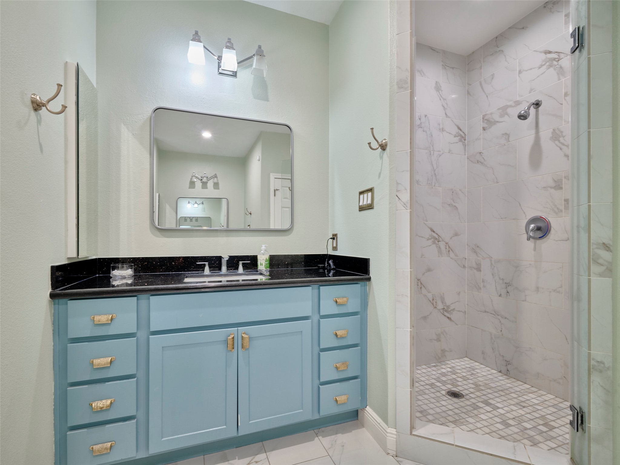 4219 Redbud Street Houston, TX 77051 - Photo 20 of 25 This bathroom features a modern design with a stylish blue vanity, sleek black countertop, and a spacious walk-in shower with elegant marble tiles.