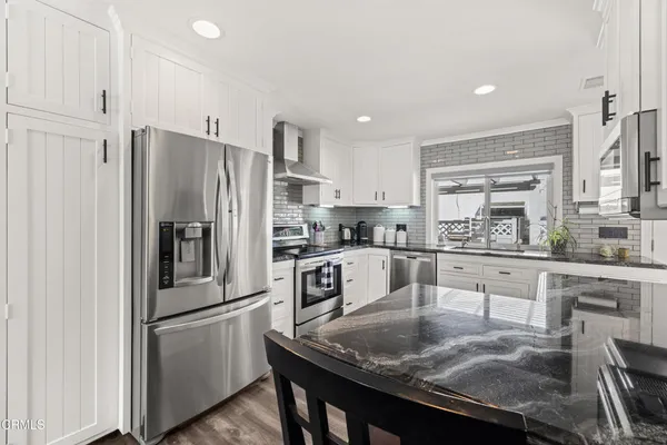 a kitchen with stainless steel appliances granite countertop a refrigerator a sink a stove a dining table and chairs