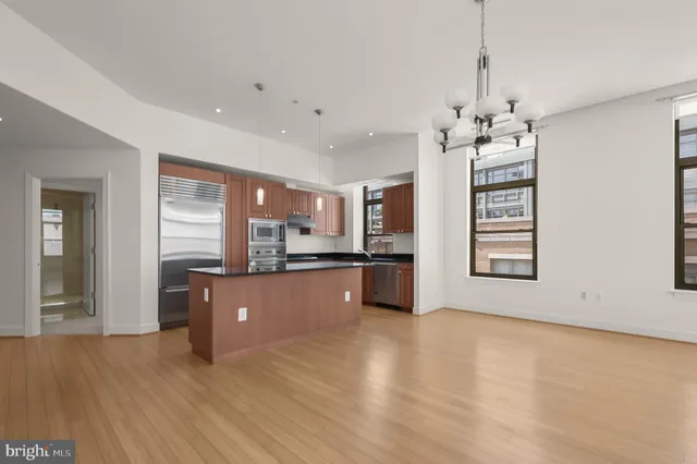 a kitchen with stainless steel appliances granite countertop a refrigerator a sink dishwasher a stove and a dining table with wooden floor