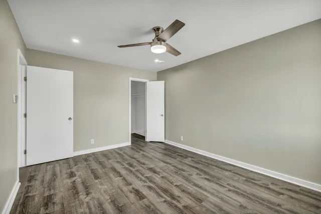a view of an empty room with wooden floor and ceiling fan