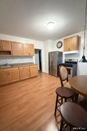 a kitchen with stainless steel appliances granite countertop a stove a sink a refrigerator white cabinets and a dining table