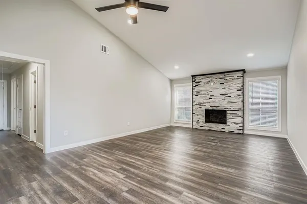 an empty room with wooden floor fireplace and windows