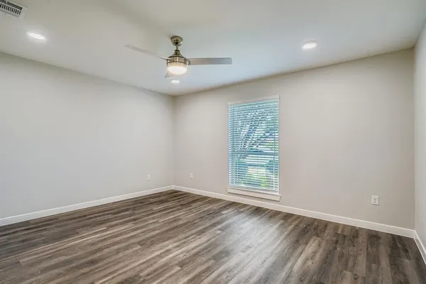 an empty room with wooden floor chandelier fan and windows