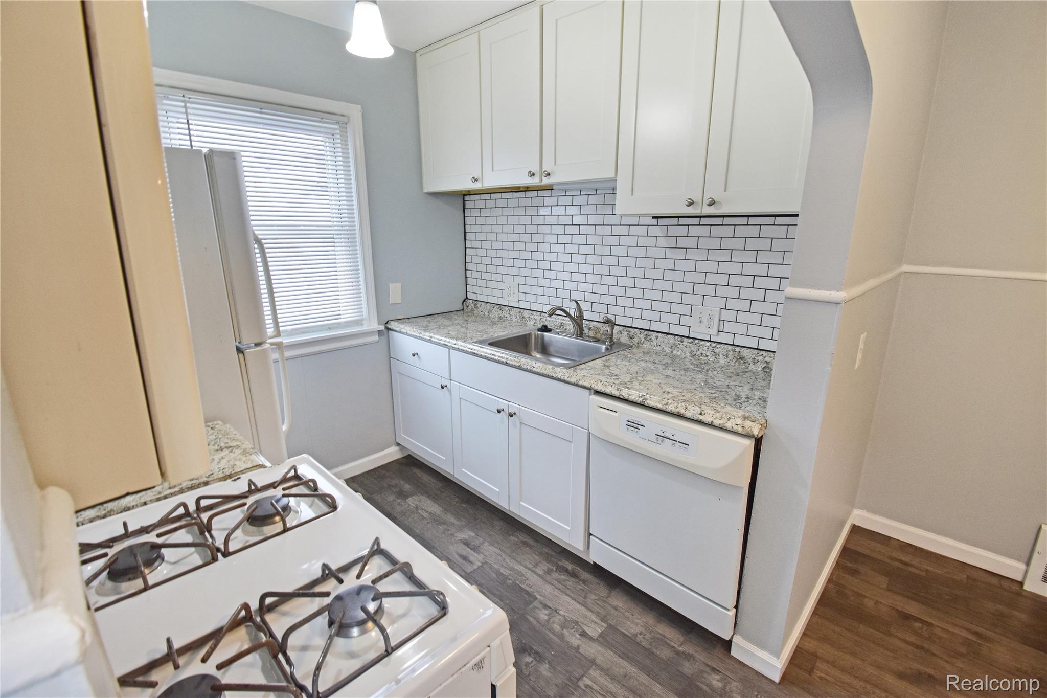 8305 Stephens Road Center Line, MI 48015 - Photo 7 of 23 Kitchen featuring white appliances, decorative backsplash, white cabinetry, and dark wood-style floors