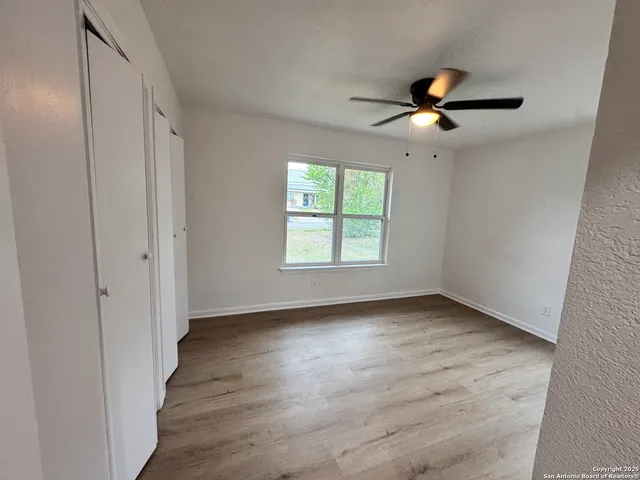 an empty room with wooden floor chandelier fan and windows