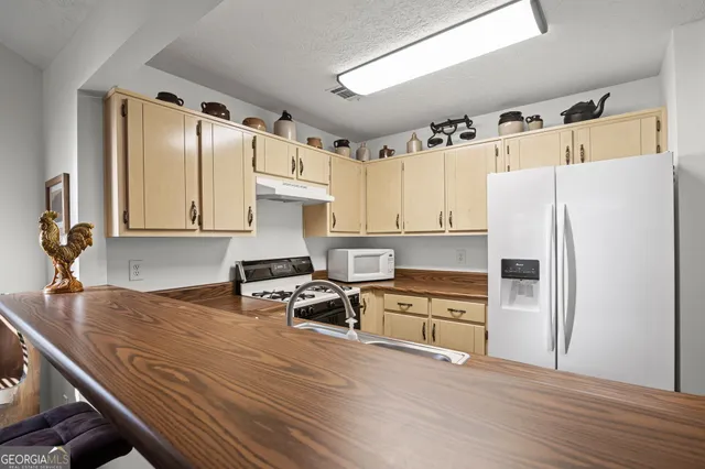 a kitchen with granite countertop a refrigerator a stove a sink and white cabinets with wooden floor