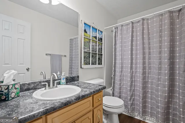 a bathroom with a granite countertop sink a toilet a mirror and shower curtain