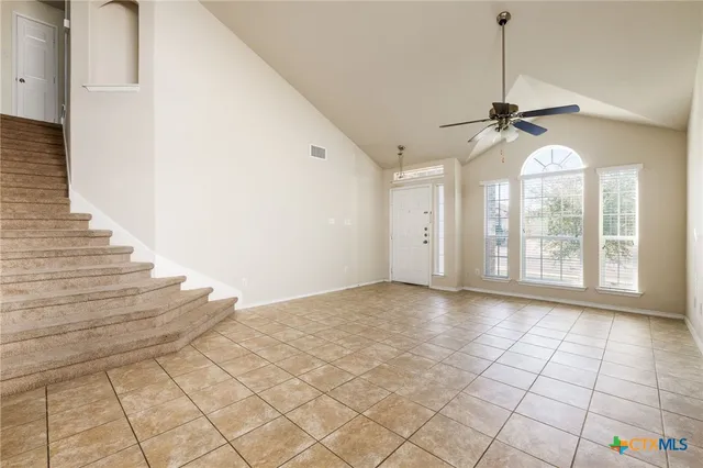 a view of an empty room with stairs and chandelier fan