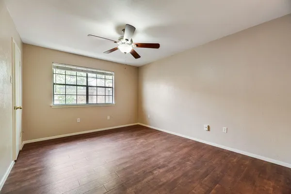 an empty room with wooden floor chandelier fan and windows
