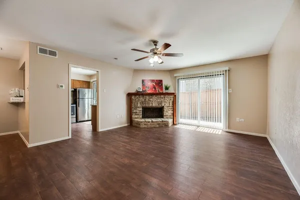 an empty room with wooden floor a ceiling fan a fireplace and windows