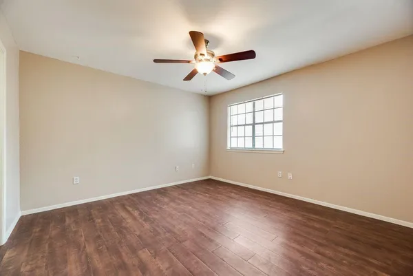 an empty room with wooden floor ceiling fan and windows