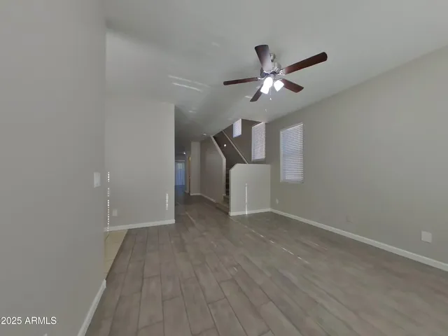 an empty room with wooden floor chandelier fan and windows