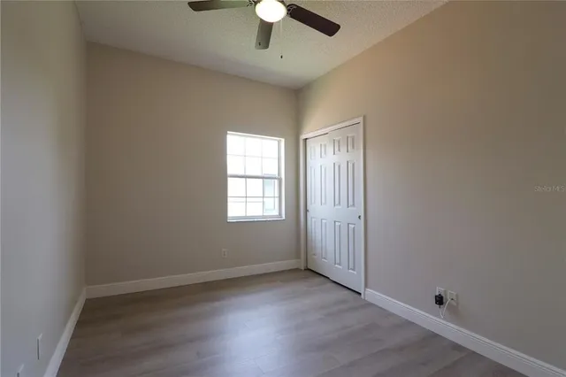 an empty room with wooden floor chandelier fan and windows