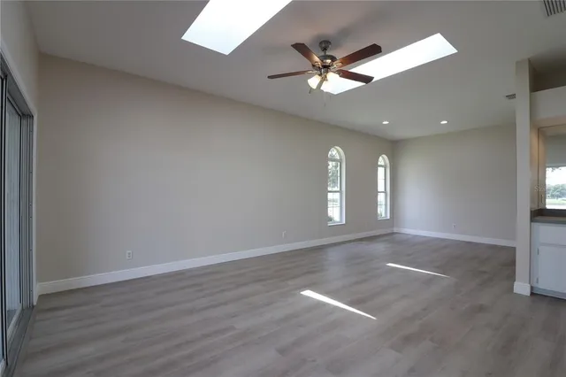 an empty room with wooden floor fan and windows