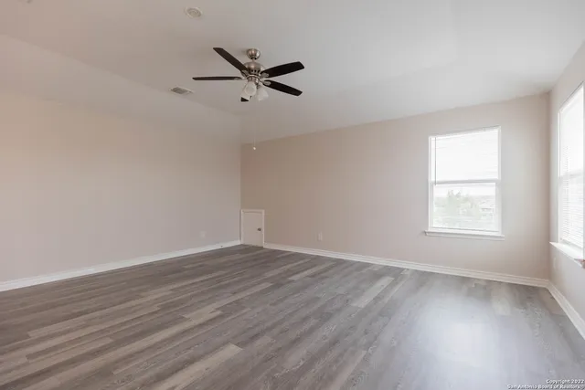 an empty room with wooden floor fan and windows