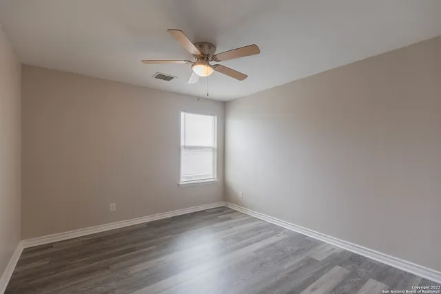 an empty room with wooden floor fan and windows