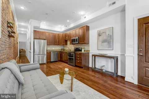 a kitchen with stainless steel appliances granite countertop a refrigerator a stove top oven a sink dishwasher and couches with wooden floor