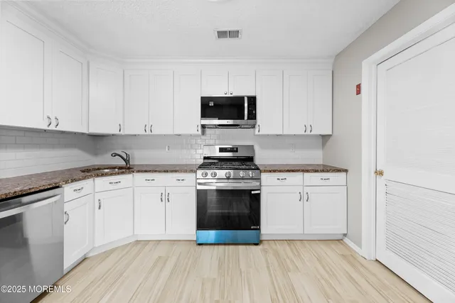 a kitchen with granite countertop a stove and white cabinets