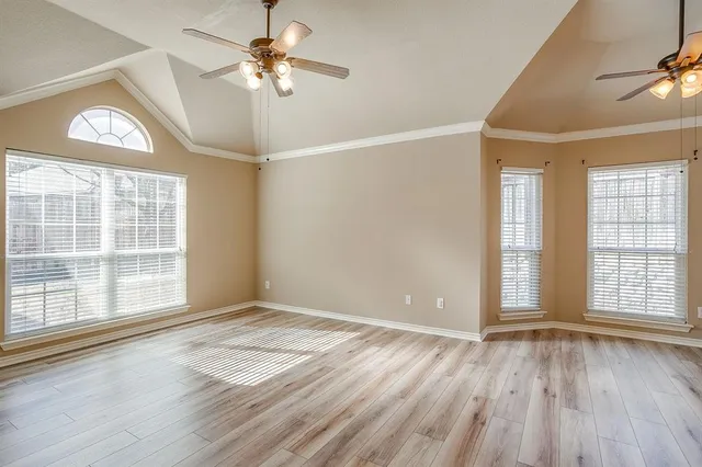 an empty room with wooden floor chandelier fan and windows