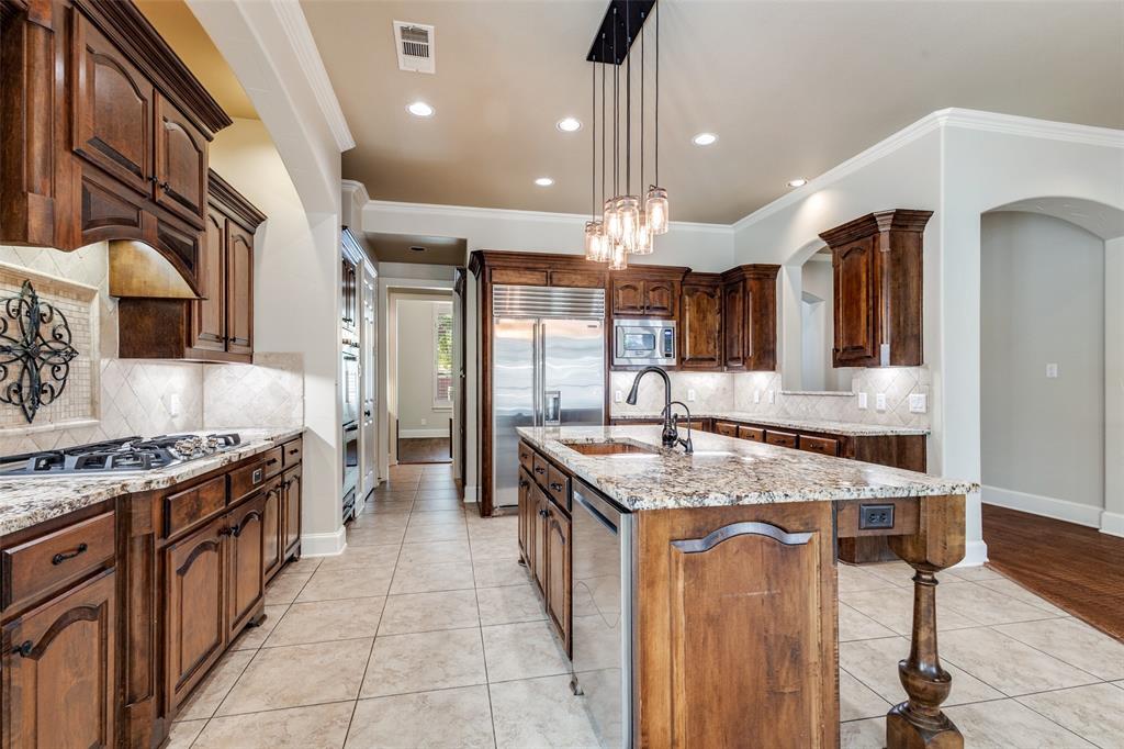 901 Sandy Trail Keller, TX 76248 - Photo 15 of 36 Kitchen with light stone counters, light tile patterned flooring, an island with sink, pendant lighting, and ornamental molding