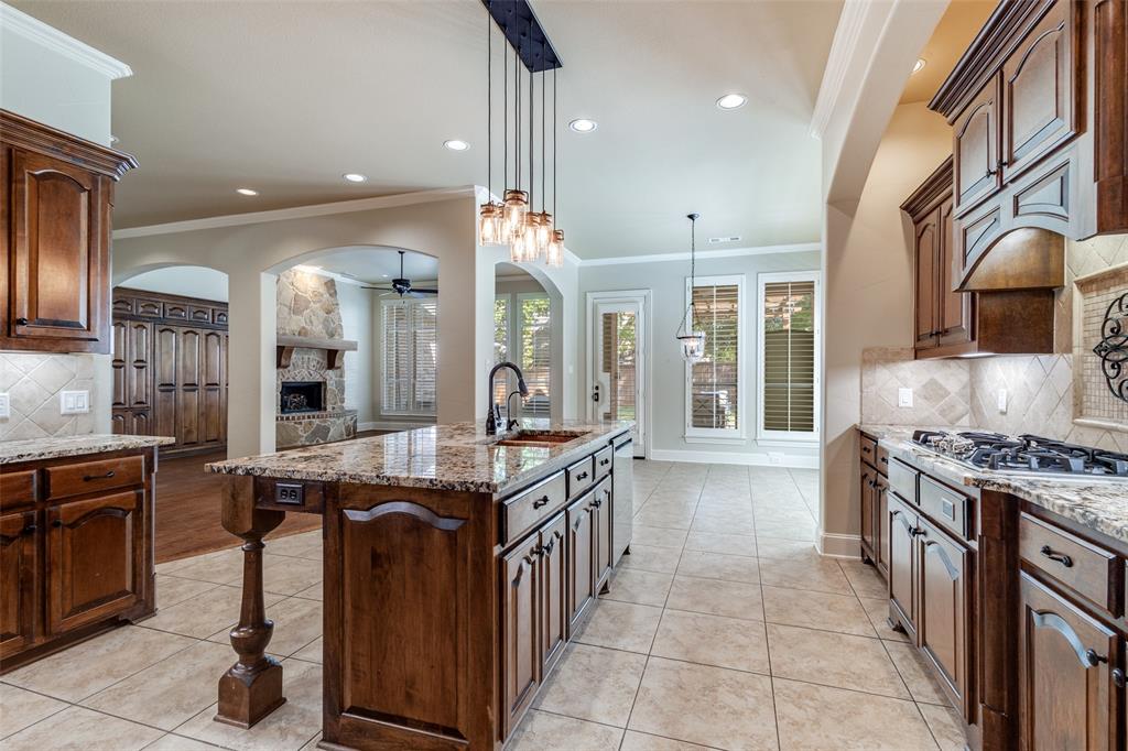 901 Sandy Trail Keller, TX 76248 - Photo 16 of 36 Kitchen with decorative backsplash, a stone fireplace, light stone counters, a ceiling fan, and crown molding