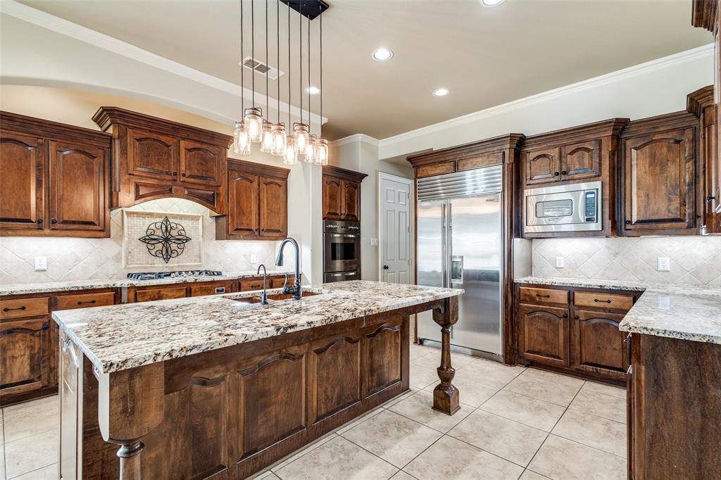 901 Sandy Trail Keller, TX 76248 - Photo 19 of 36 Kitchen featuring light stone counters, decorative backsplash, a kitchen island with sink, hanging light fixtures, and a breakfast bar