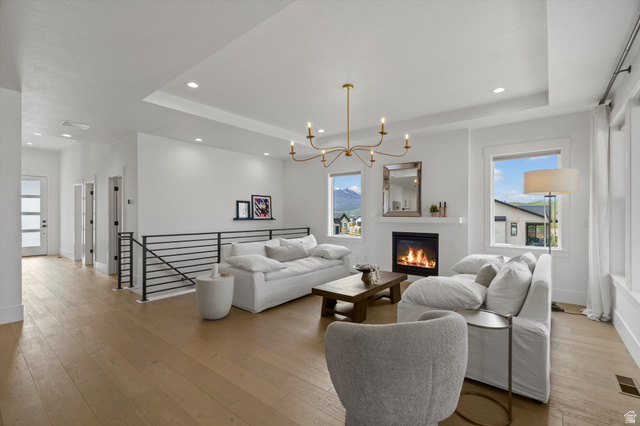 3349 Oxford Loop Morgan, UT 84050 - Photo 13 of 47 Living room with suspended lighting, healthy amount of natural light, a tray ceiling, light wood finished floors, and a glass covered fireplace