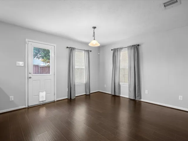 an empty room with wooden floor chandelier and windows