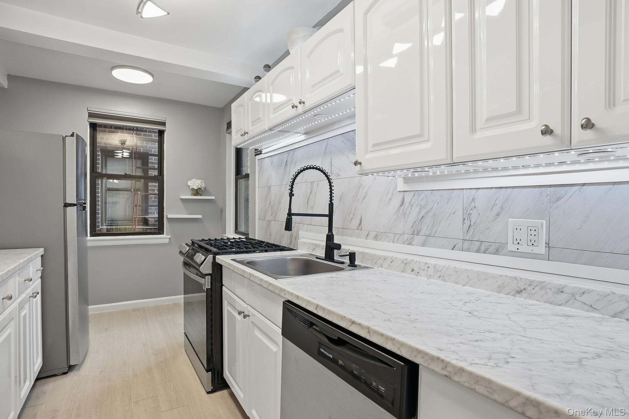 Renovated eat-in Kitchen with white cabinetry, stainless steel appliances,  designer lighting