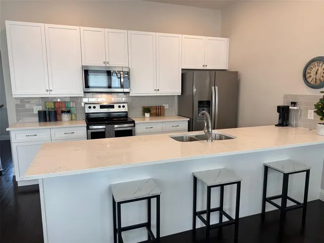 a kitchen with stainless steel appliances a stove a sink a microwave a refrigerator and white cabinets