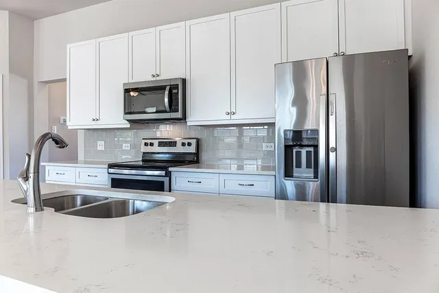 a kitchen with stainless steel appliances a refrigerator a sink a stove and white cabinets