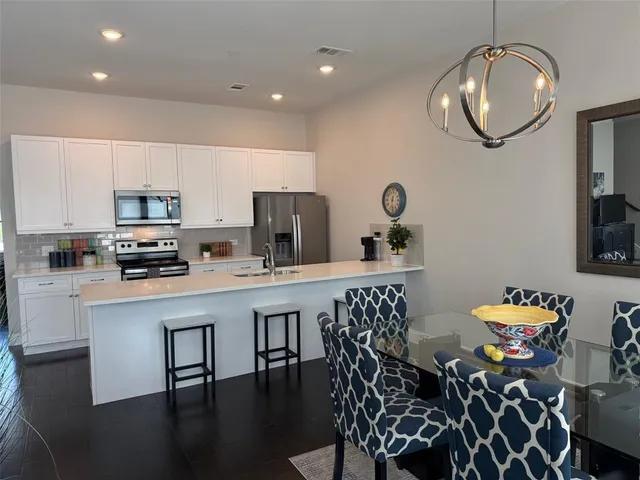 a kitchen with stainless steel appliances granite countertop a dining table chairs a microwave a refrigerator and a stove