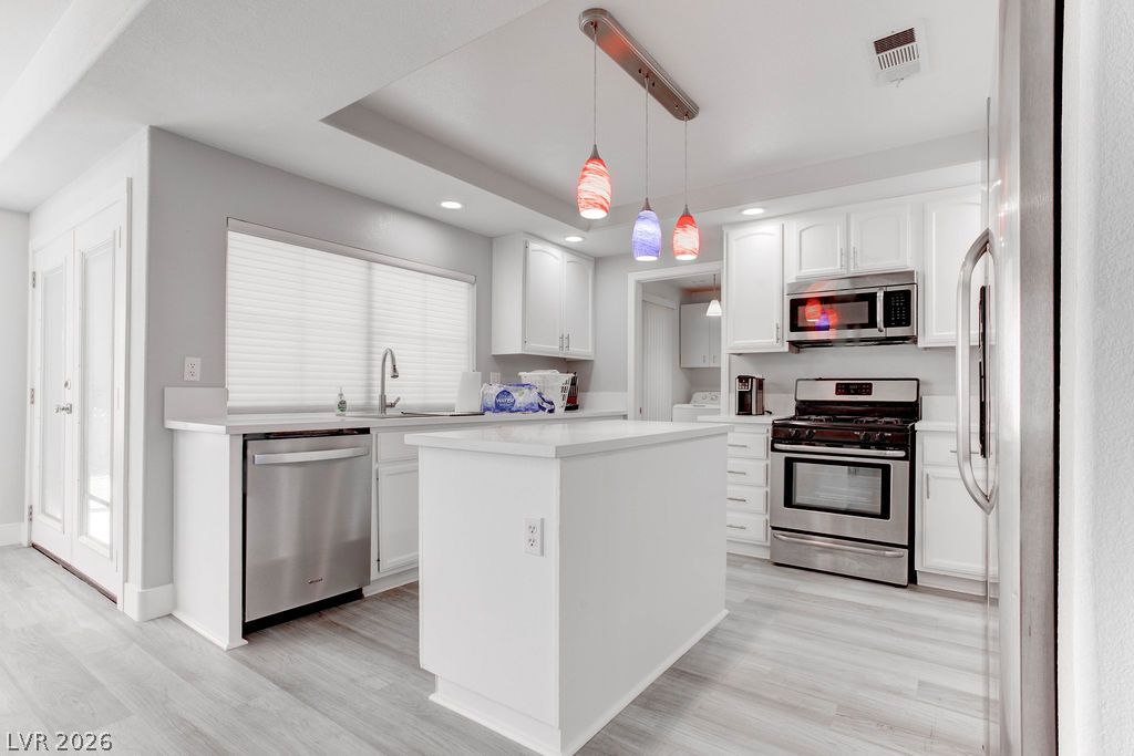1 Rising Sun Court Henderson, NV 89074 - Photo 8 of 47 A pristine white kitchen featuring sleek stainless steel appliances and a stylish island with pendant lighting.