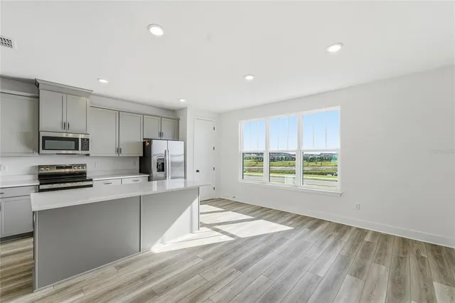 a large kitchen with stainless steel appliances granite countertop a stove a sink a refrigerator white cabinets and a wooden floor