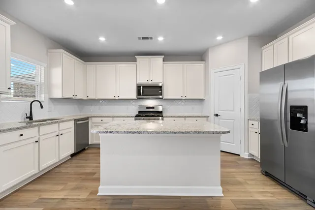 a large kitchen with stainless steel appliances granite countertop a stove a sink dishwasher a refrigerator and white cabinets with wooden floor