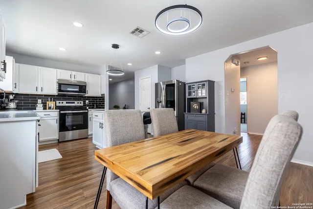 a kitchen with stainless steel appliances granite countertop a refrigerator a stove top oven a sink dishwasher a dining table and chairs with wooden floor