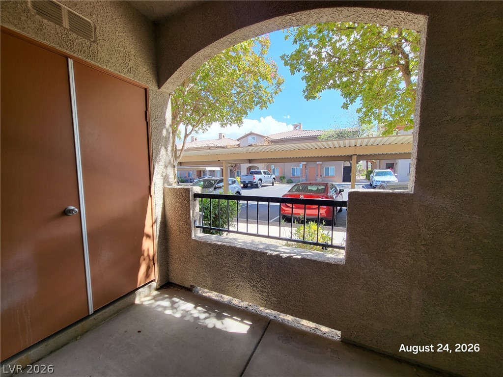 7701 West Robindale Road, Unit 125 Las Vegas, NV 89113 - Photo 15 of 16 A covered concrete balcony looks out toward the parking area through a wide arched opening.