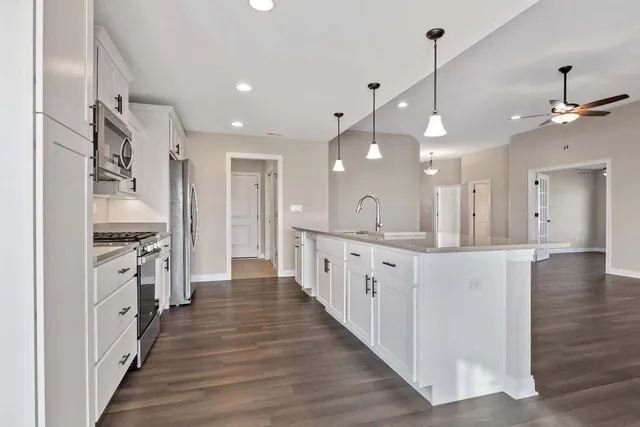 a large kitchen with granite countertop a large center island a sink dishwasher and a stove with wooden floor