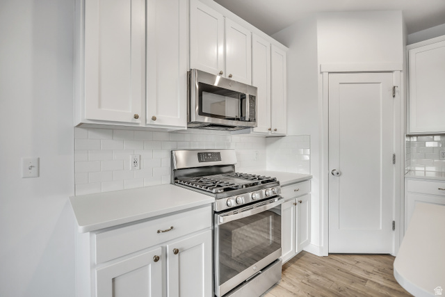 1058 Lilac Way Mapleton, UT 84664 - Photo 6 of 28 Kitchen featuring appliances with stainless steel finishes, white cabinetry, light wood-style flooring, and decorative backsplash