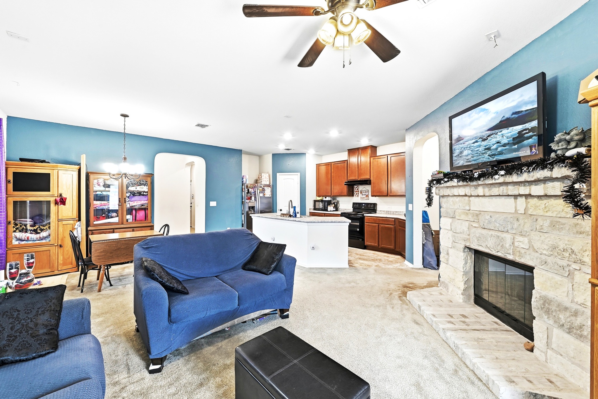 1621 Dragonfly Loop Bastrop, TX 78602 - Photo 6 of 27 Open-concept living space featuring a stone fireplace, integrated kitchen with wood cabinetry, a ceiling fan, and carpet flooring