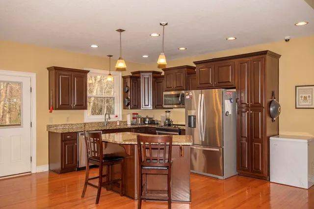 a kitchen with stainless steel appliances a refrigerator a stove a sink a dining table and chairs with wooden floor