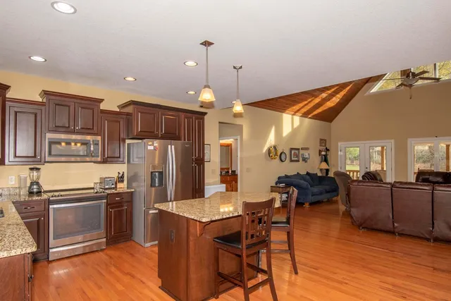 a kitchen with stainless steel appliances kitchen island granite countertop a refrigerator a stove a sink a dining table and chairs with wooden floor