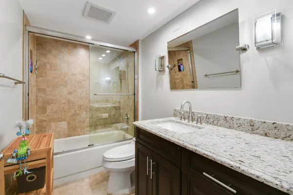 a bathroom with a granite countertop sink a toilet a mirror a vanity and bathtub