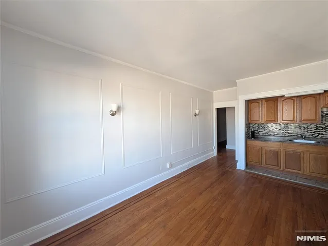 a view of an empty room and kitchen with wooden floor