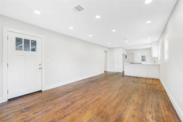 a view of an empty room with wooden floor and kitchen