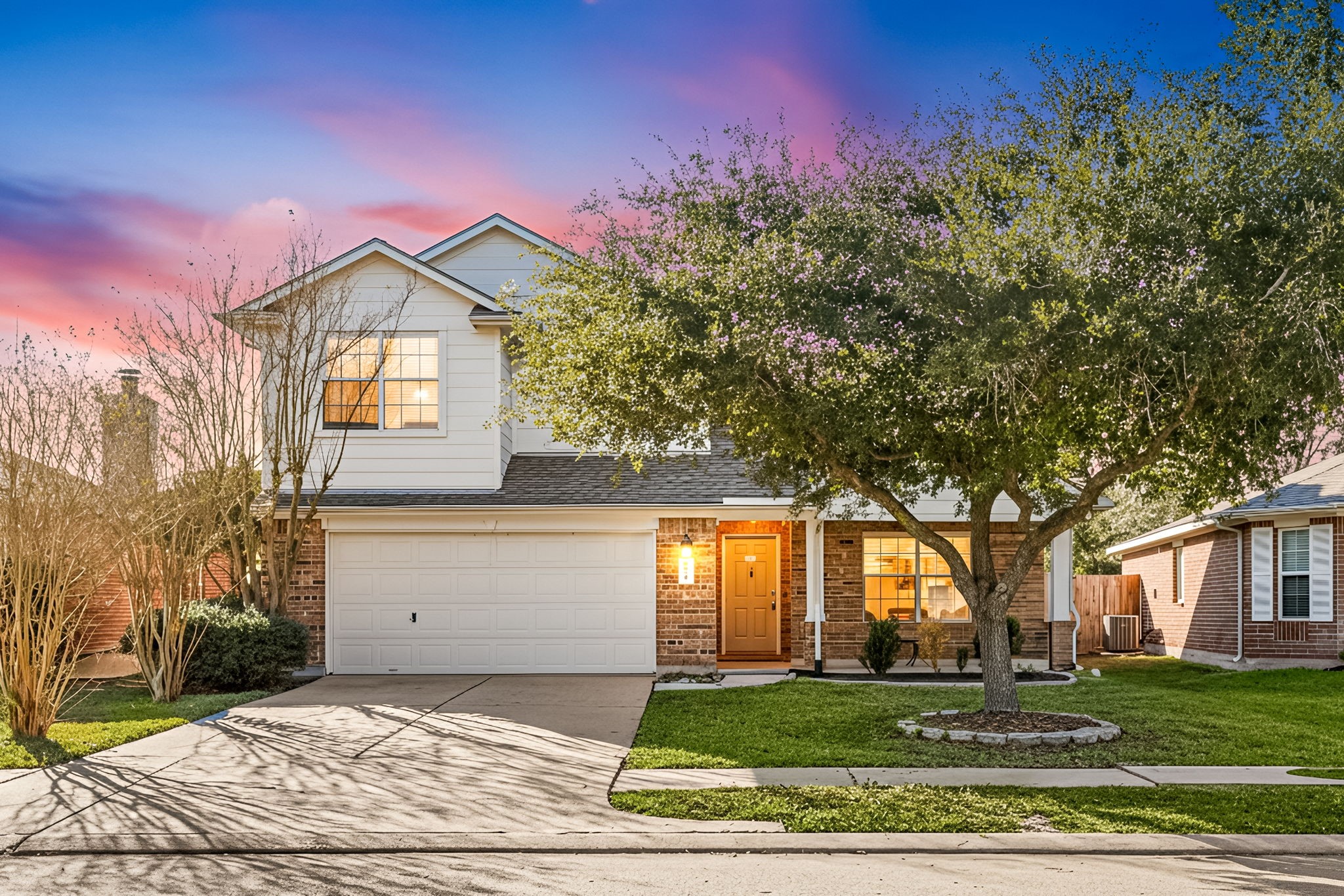 This charming two-story home features a welcoming brick exterior with a double garage and a spacious driveway. A mature tree and well-maintained landscaping enhance its curb appeal.