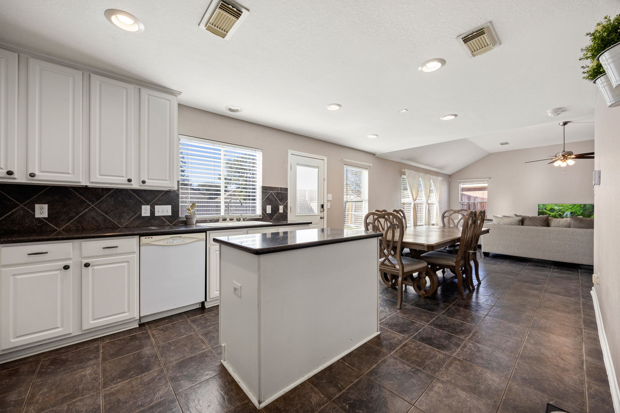 25515 Twister Trail Spring, TX 77373 - Photo 14 of 33 This photo showcases an open-concept kitchen and living area. The kitchen features white cabinetry, a central island, and granite countertops. Natural light streams in through large windows, creating a bright and welcoming atmosphere.