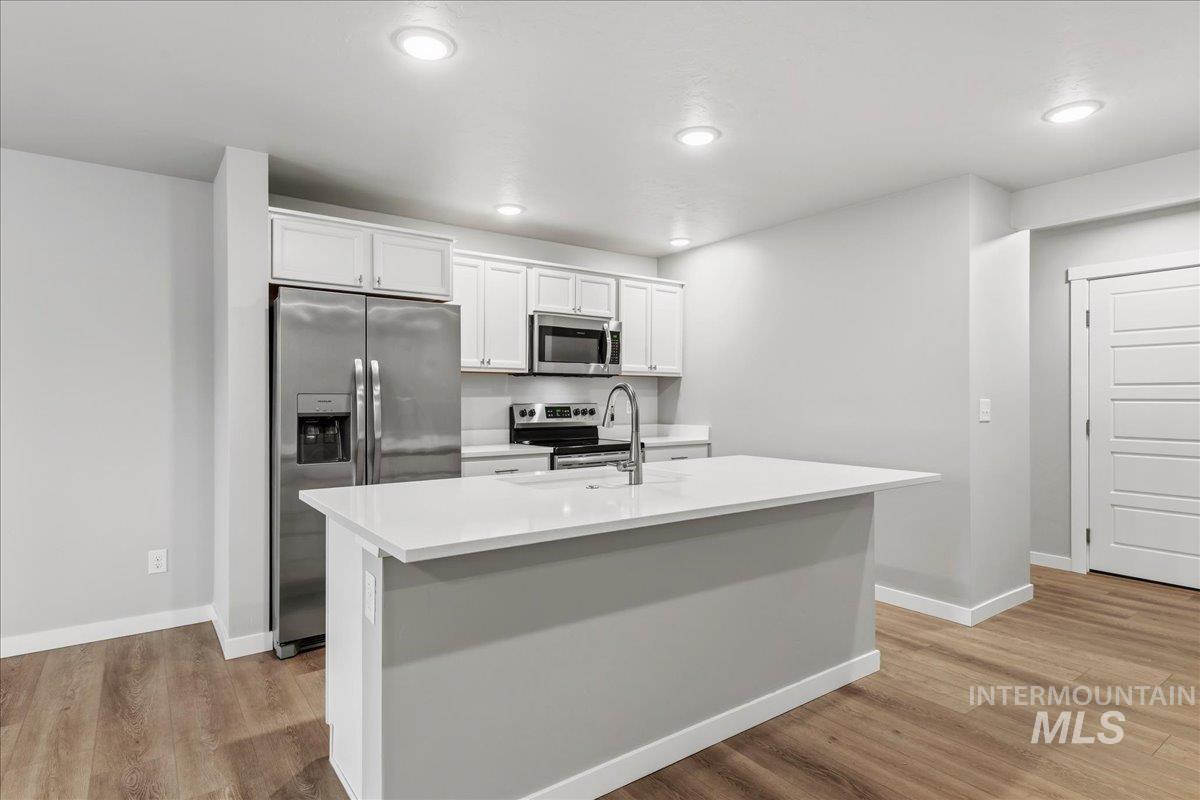 12475 West Victory Road Boise, ID 83709 - Photo 11 of 26 Kitchen featuring white cabinetry, stainless steel appliances, a center island with a white countertop, and wood-finish flooring